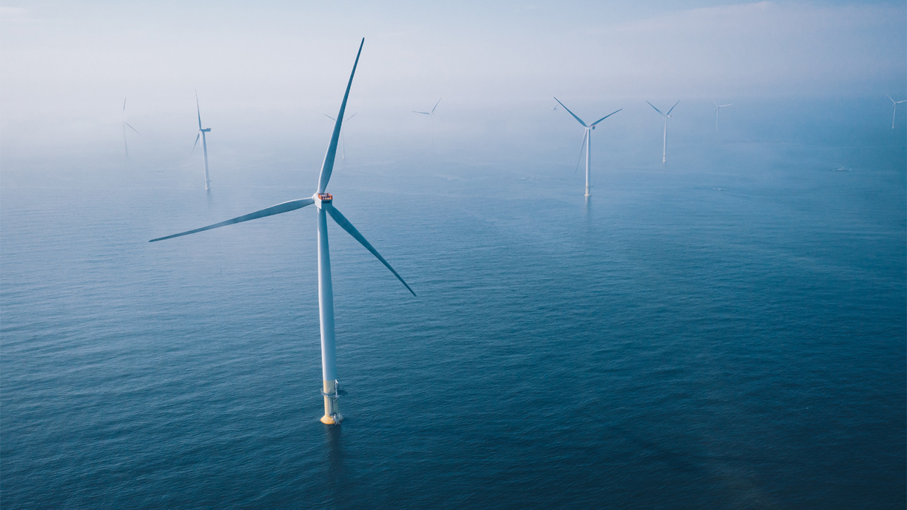 A misty aerial view of offshore wind turbines against the sea