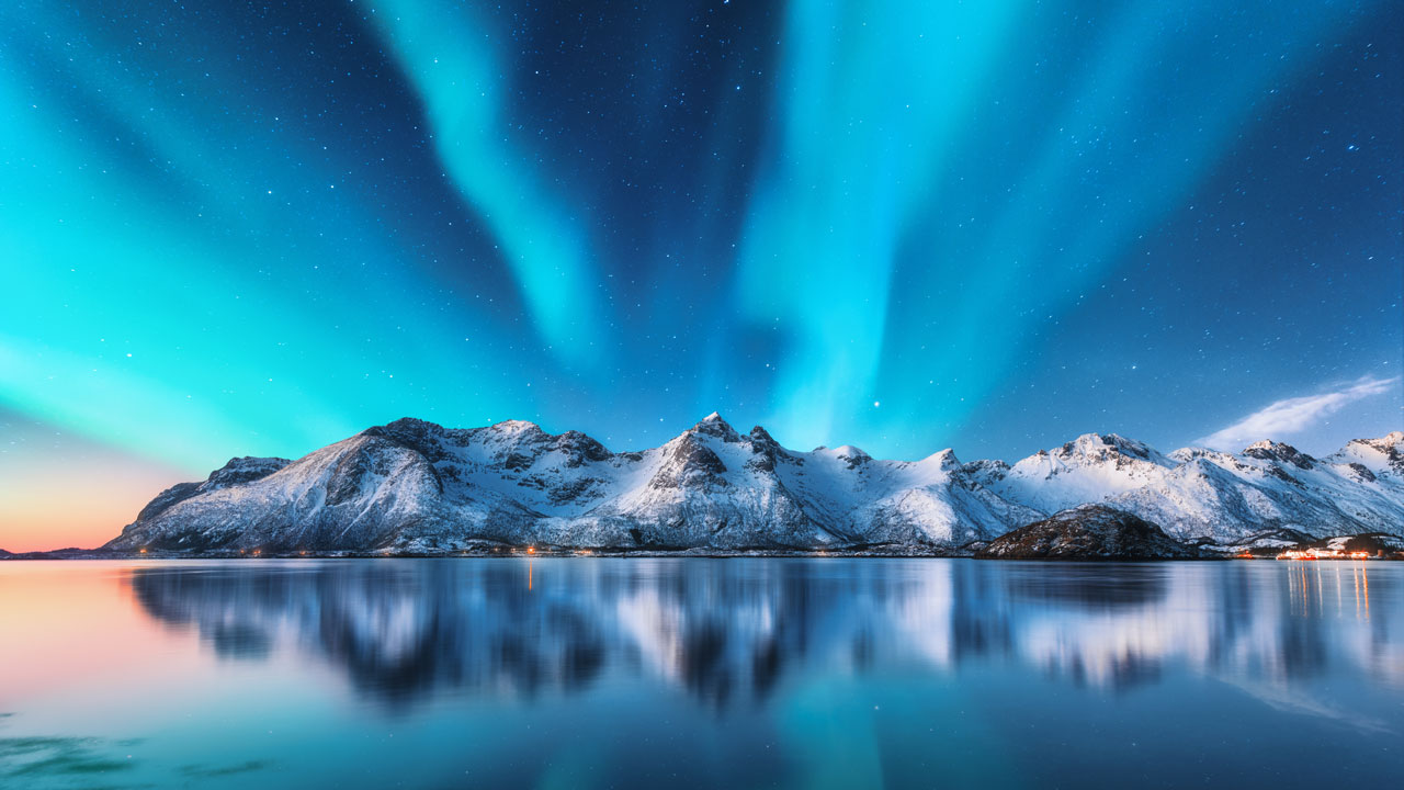 Aurora Borealis above snow-covered mountains with sea in the foreground
