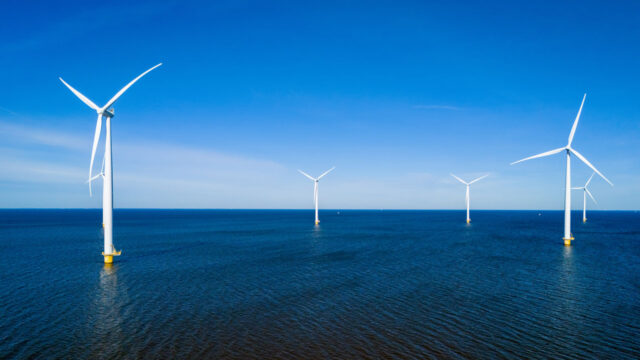 Offshore wind turbines in a calm, deep blue sea against a blue sky