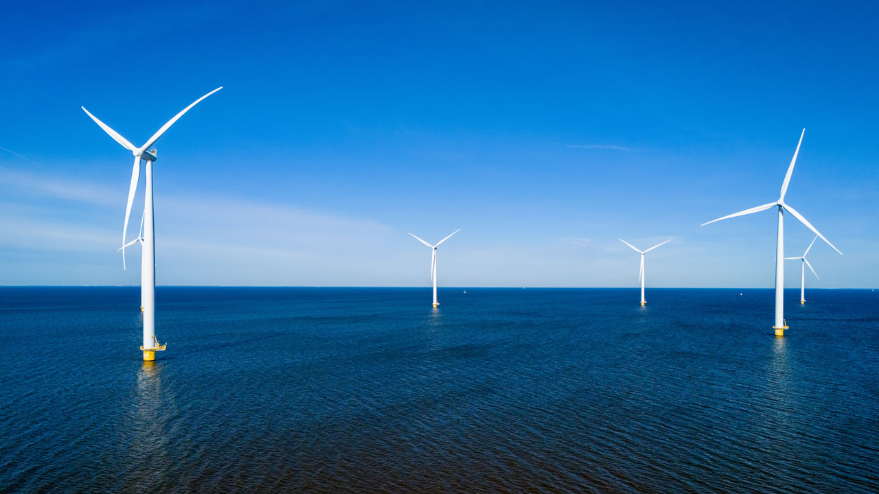 Offshore wind turbines in a calm, deep blue sea against a blue sky