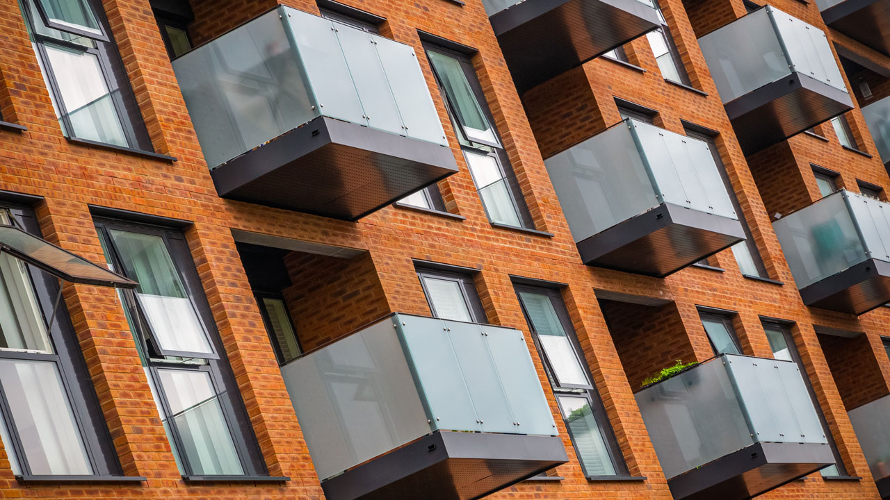 Brick apartment facade with repeating glass-railed balconies and vertical windows