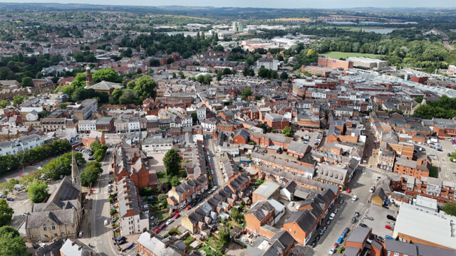 Aerial view of a town centre showing a church, residential and commercial streets with an industrial site in the background and green fields on the horizon