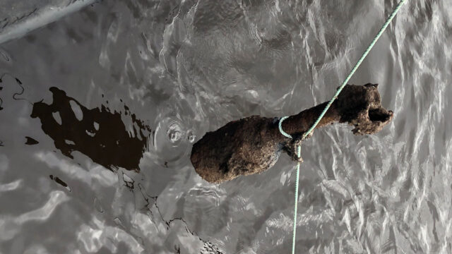 Degraded World War II unexploded bomb being pulled out of the sea on a rope
