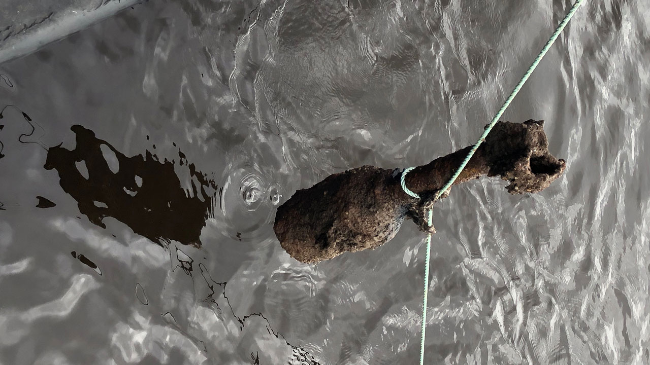 Degraded World War II unexploded bomb being pulled out of the sea on a rope