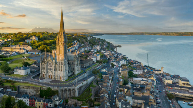 Aerial view of a seaside town looking across a bay with a large stone gothic church in the foreground and hills and green fields in the distance