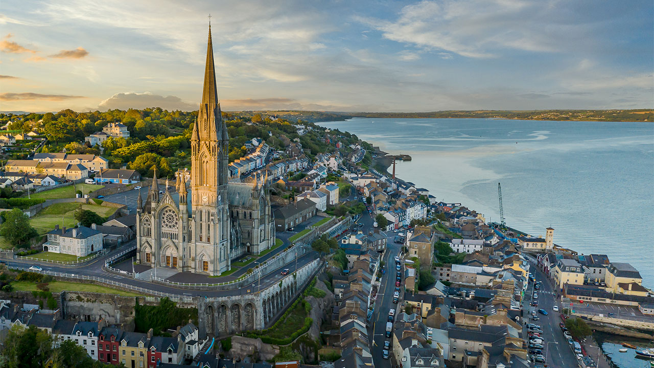 Aerial view of a seaside town looking across a bay with a large stone gothic church in the foreground and hills and green fields in the distance