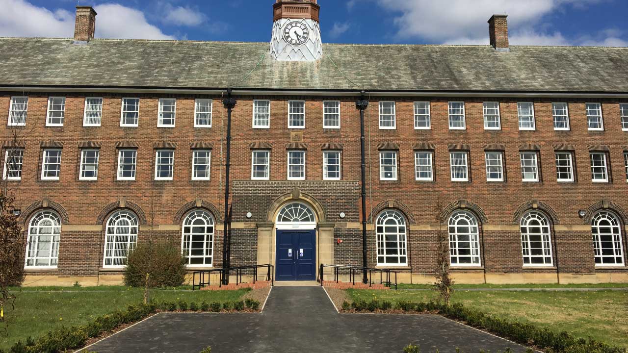 Front view of a historic brick building featuring a clock tower and large arched windows