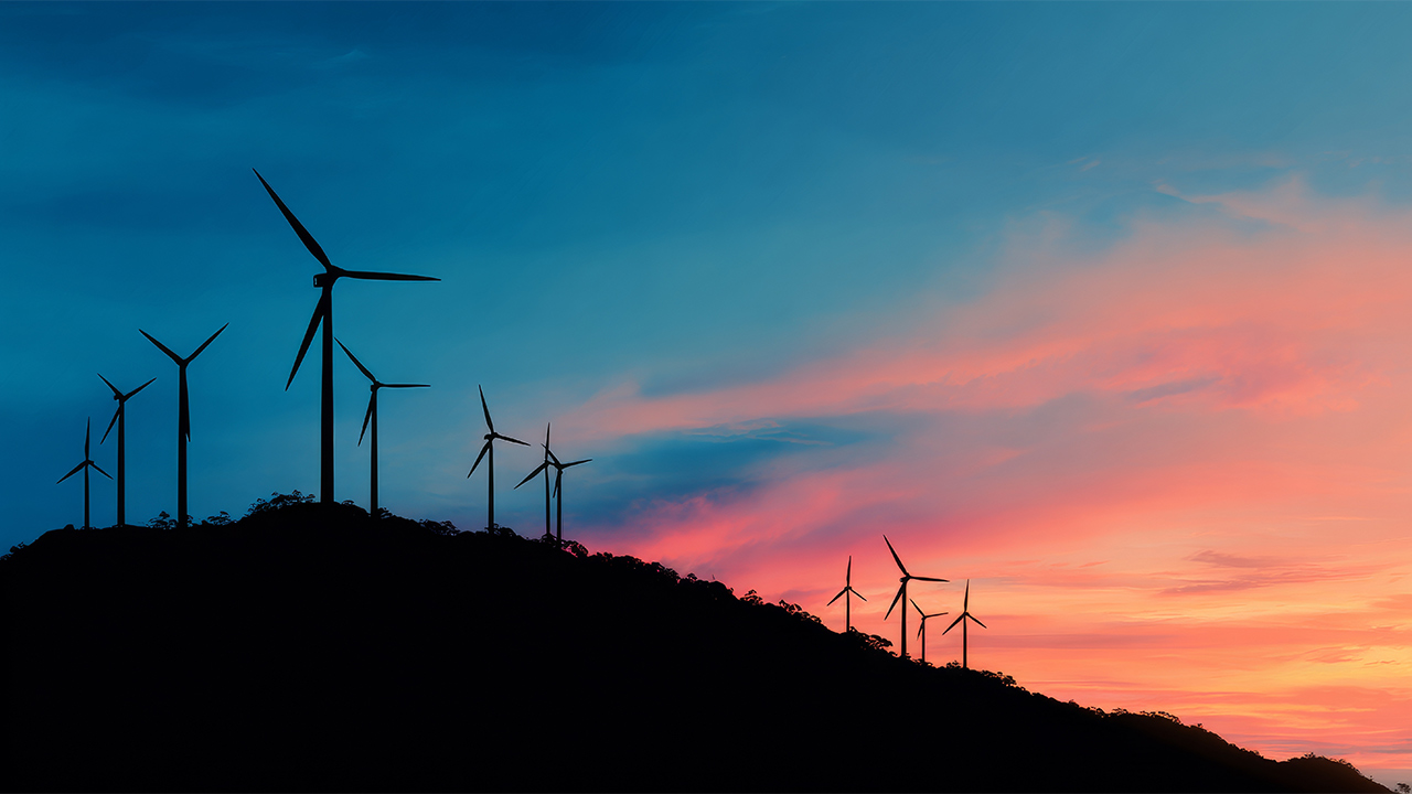 Silhouetted wind turbines along a ridgeline against a vivid pink-and-blue sunset sky