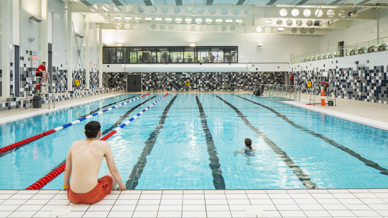 An indoor swimming pool with clear blue water, lane dividers, and a lifeguard on duty