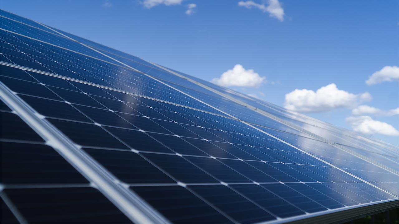 Close up view looking over ground-mounted solar panels against a blue sky