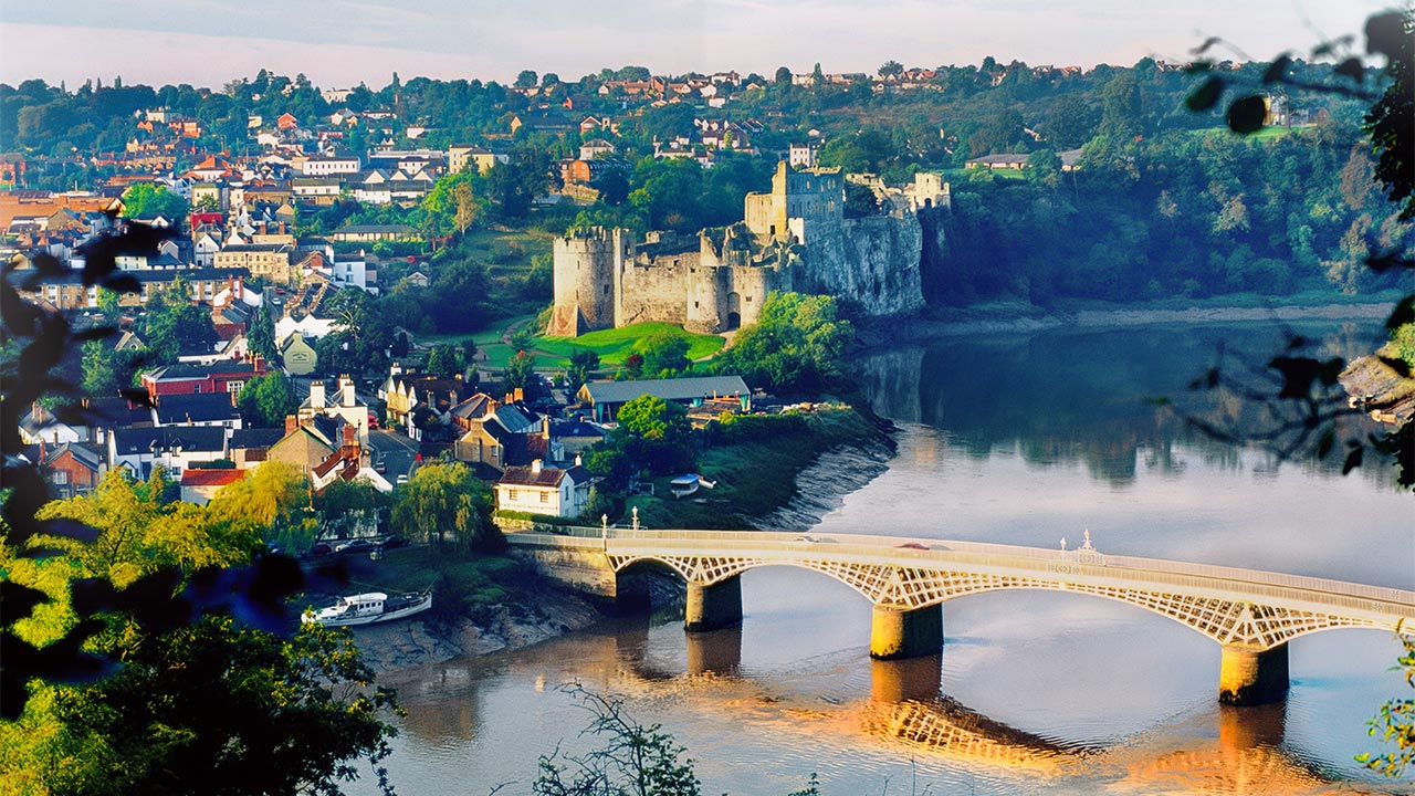 A view across the river in Chepstow showing a bridge across the river, the castle on the river bank and the town behind