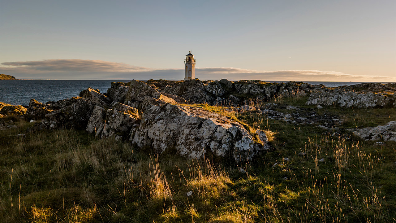 A view across a rock outcrop towards the sea with a lighthouse in the distance