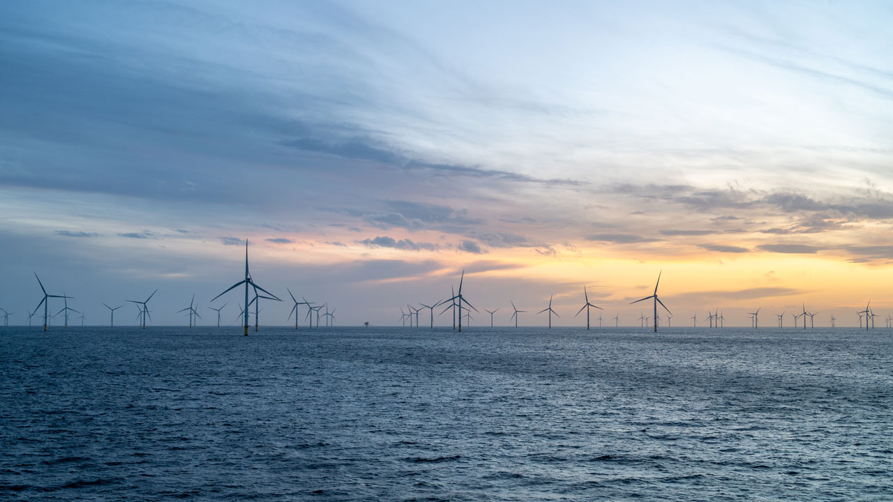Offshore wind turbines against a stormy sky at sunset