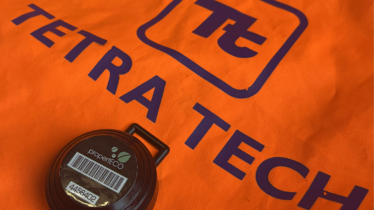 A close-up of a round device labeled "propertECO" on an orange bag with the Tetra Tech logo