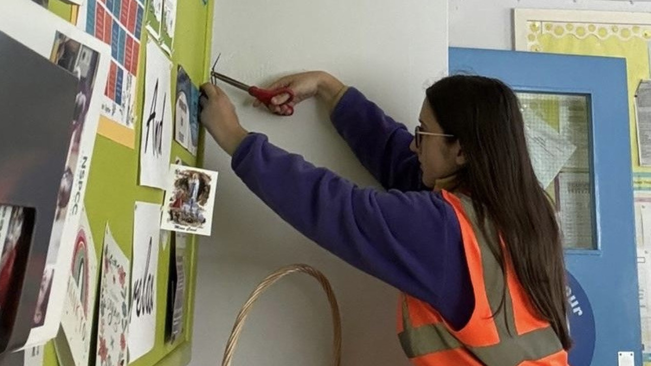 A person wearing an orange safety vest using scissors to cut a string attached to a bulletin board