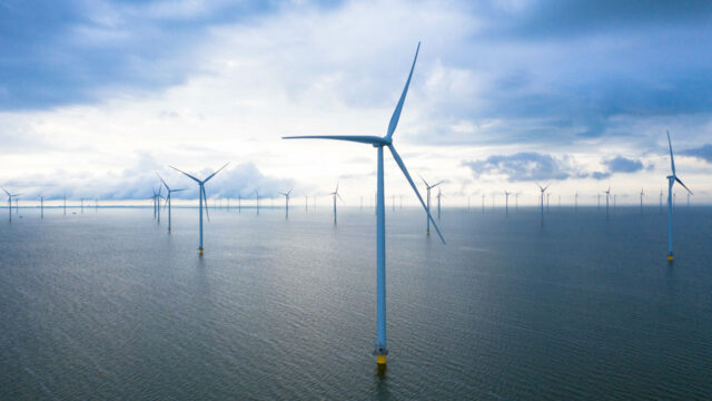 A view of offshore wind turbines against a calm sea and a blue sky