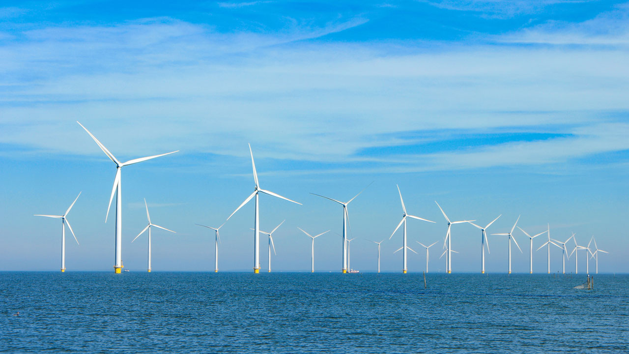 Multiple offshore wind turbines against the horizon with sea in the foreground