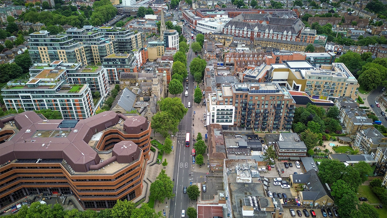 Aerial view of a town centre showing a central tree-lined road with modern office buildings on either side interspersed with older buildings and a church with a tall spire