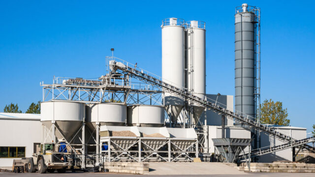 Industrial buildings against a blue sky showing large grey storage tanks and hoppers
