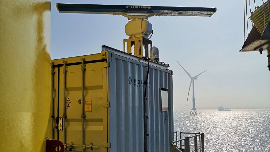 Close up of a large grey steel box containing monitoring equipment on the platform at the base of a wind turbine