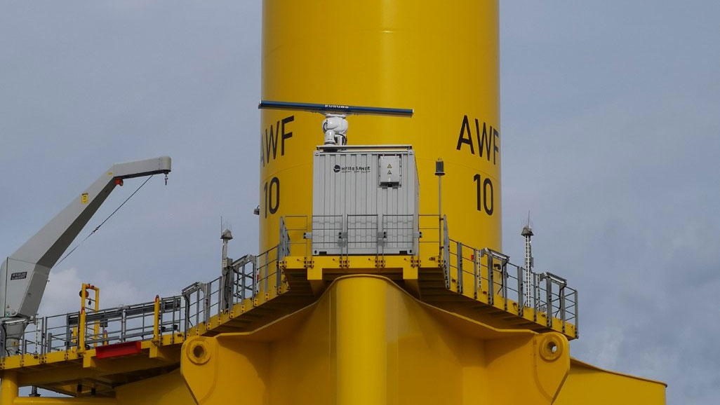 Close-up of the base of a wind turbine showing a large grey monitoring box in the foreground