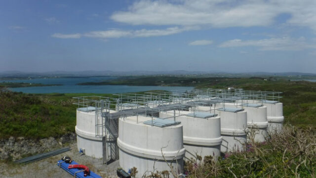 Large white water treatment tanks in the foreground with a water reservoir in the distance
