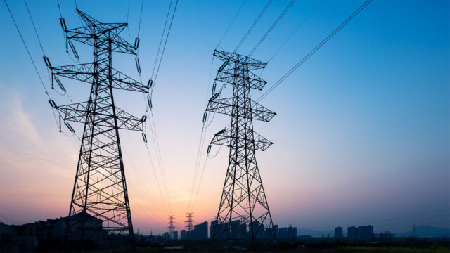 A photograph looking up at two electrical poles with a distant cityscape in the background