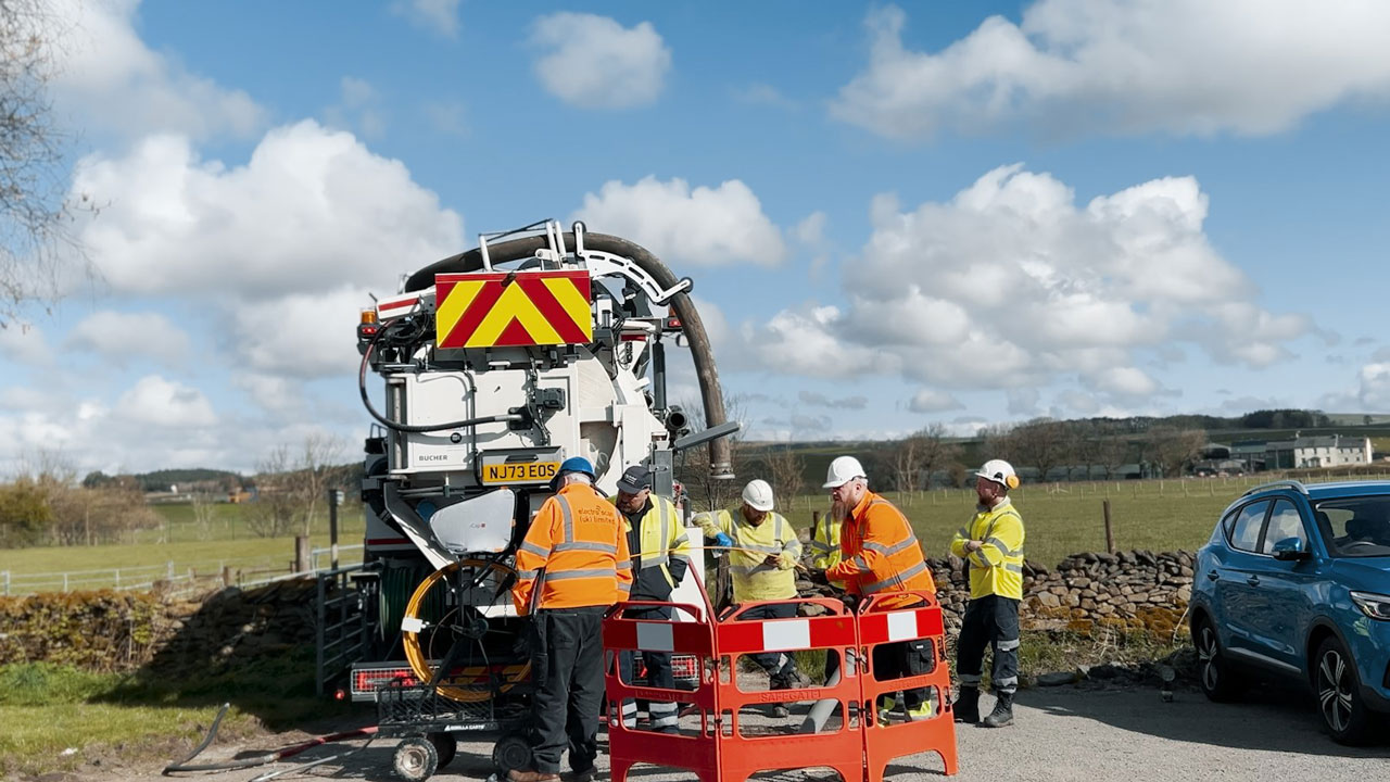 Group of workers at the side of a road with machinery behind them and a field and a cloudy sky in the background