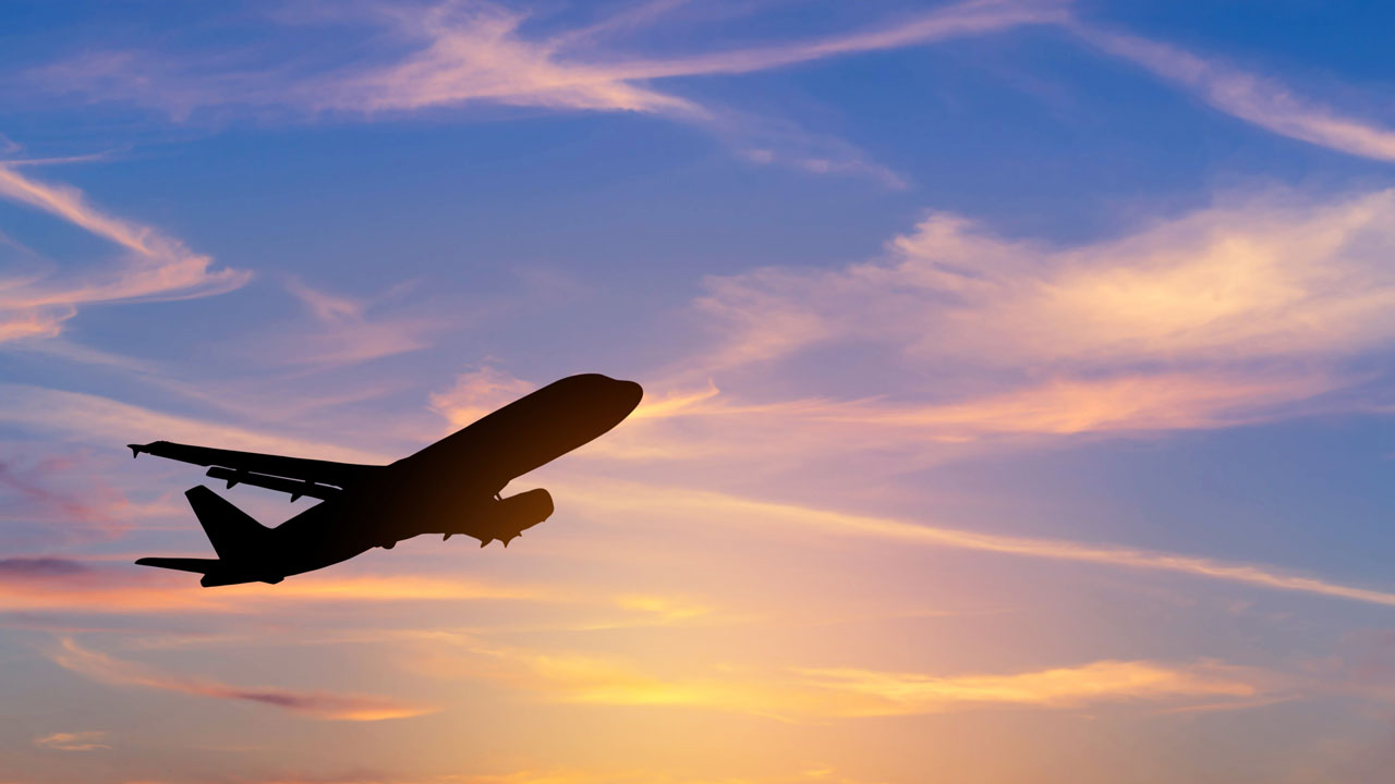 Silhouetted passenger airplane flying at high altitude against a sunset