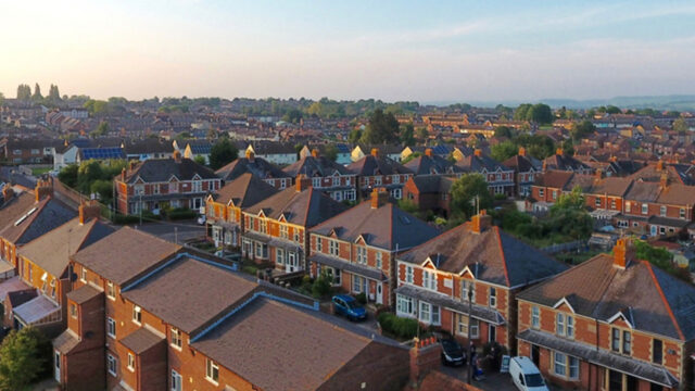 Aerial view of a residential neighbourhood with rows of brick houses under a blue sky at sunset.