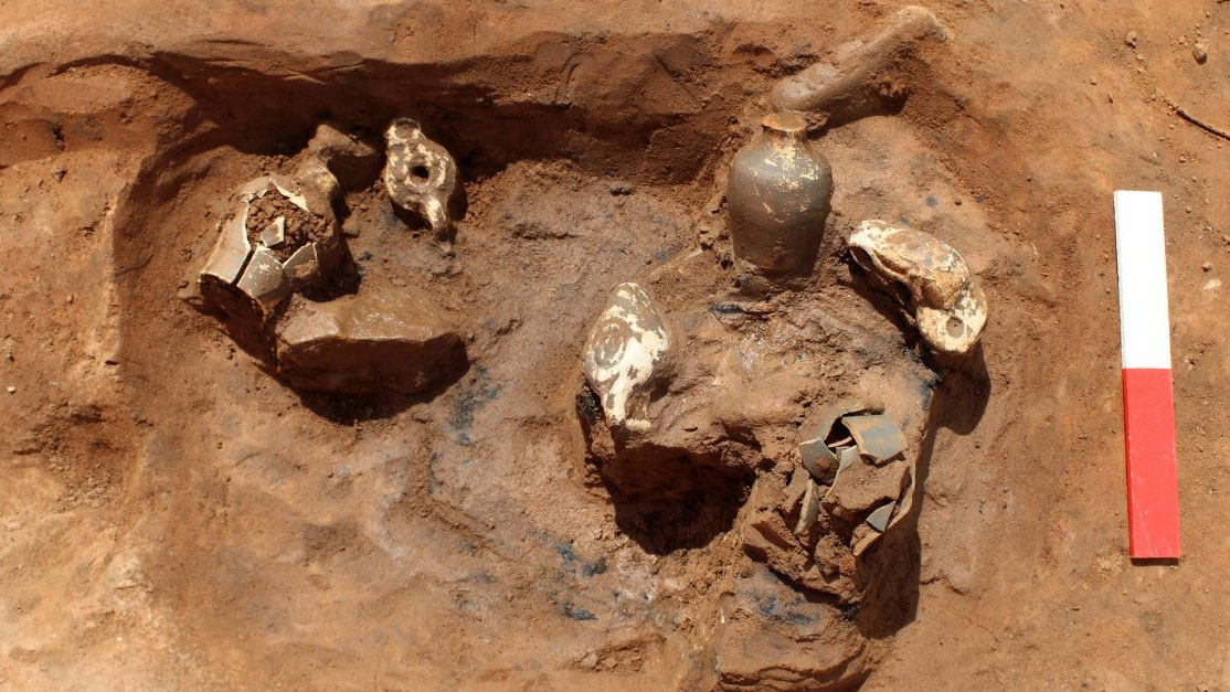 An archaeological excavation pit containing several ancient pottery fragments and a small intact vessel