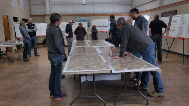 Photo of several people looking at large documents and maps laying on several tables