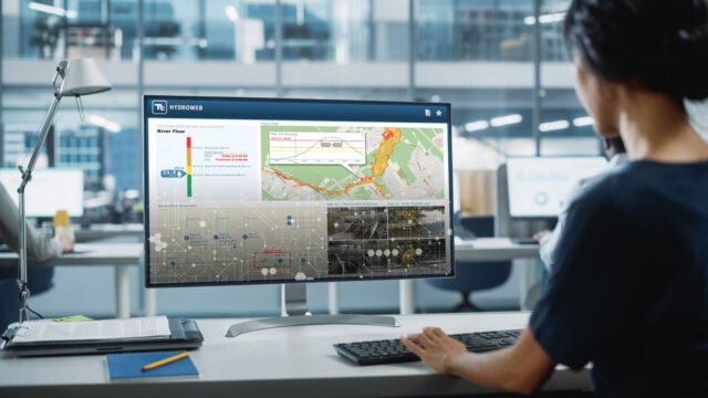 Person typing at a desk while viewing the HydroWeb platform on a desktop monitor