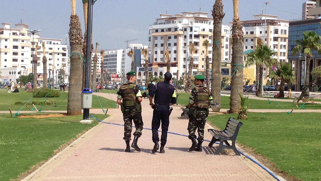 Image of three people walking down a path in a grassy park, two wearing camouflage outfits