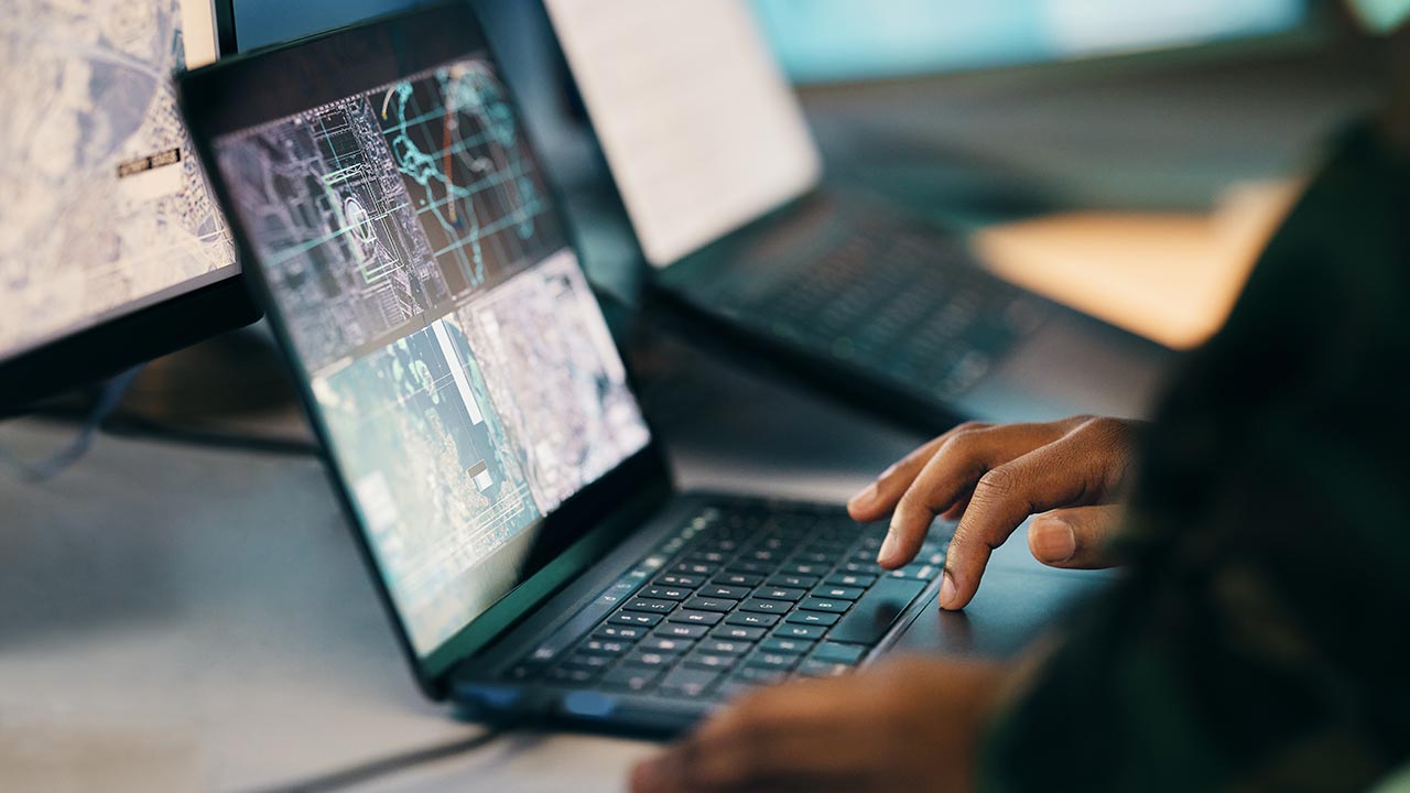 A closeup view of a person using a laptop displaying four digital map visuals