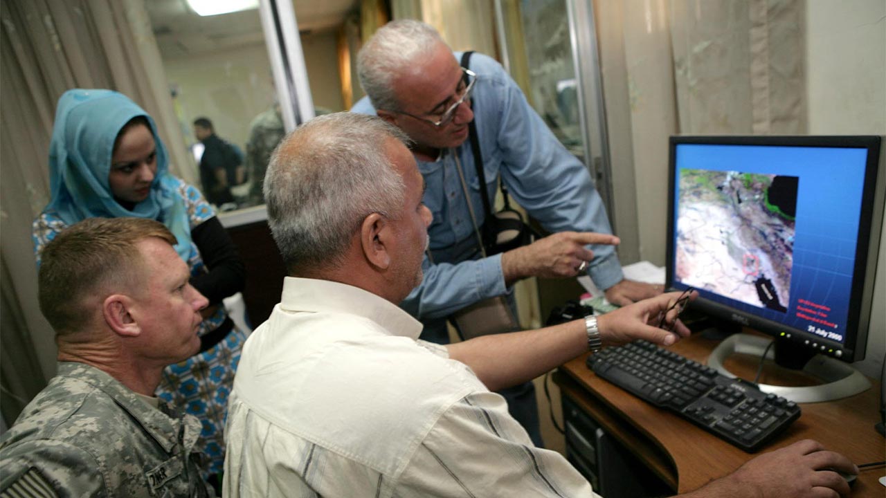 A group of people sit and stand around looking at a desktop computer