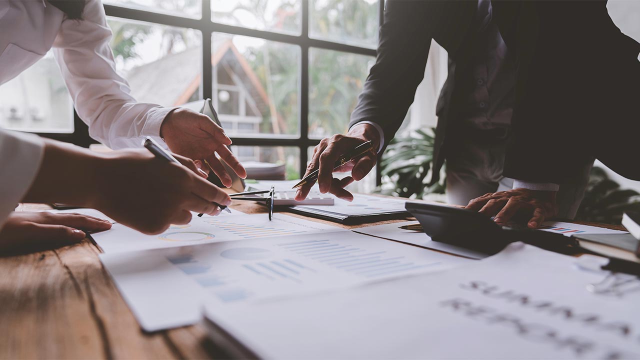 Image of people at a table pointing to paper documents