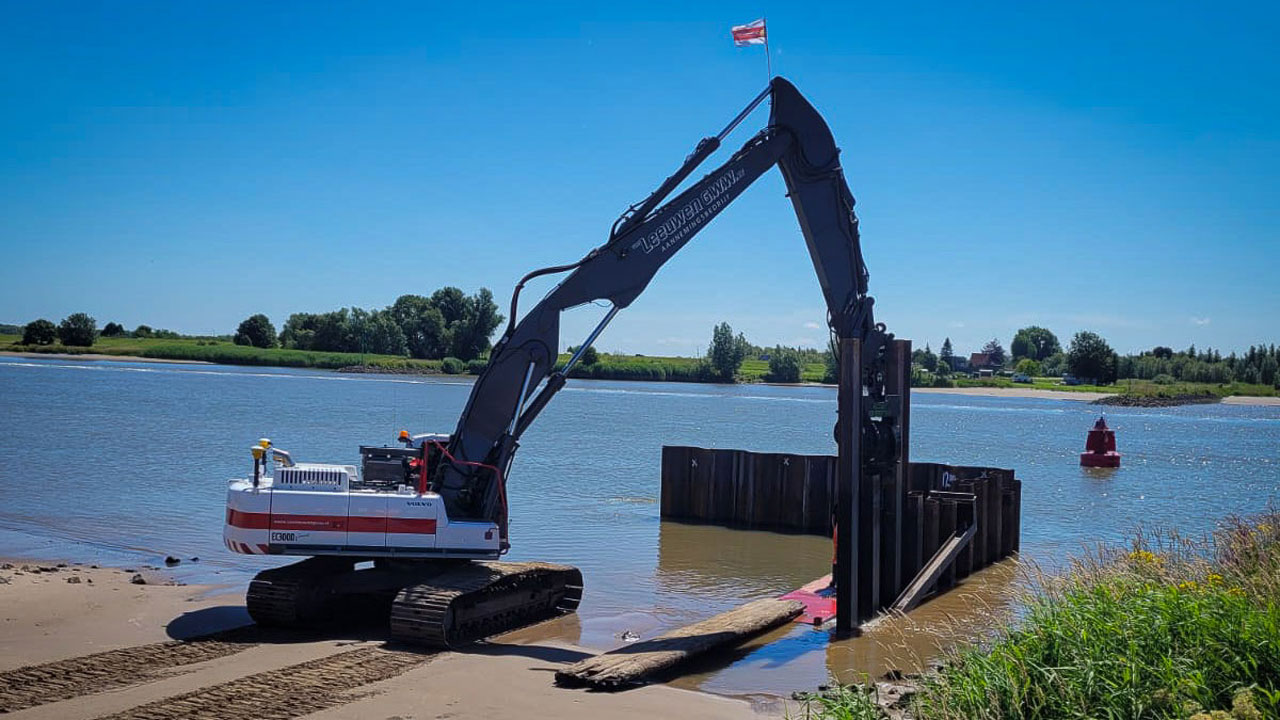 Digger equipment works at the water line with a blue sky in the background