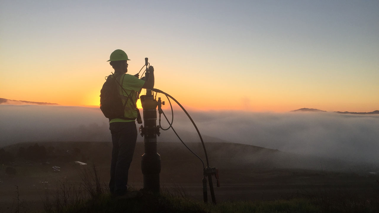 Technician inspecting landfill gas well at sunset