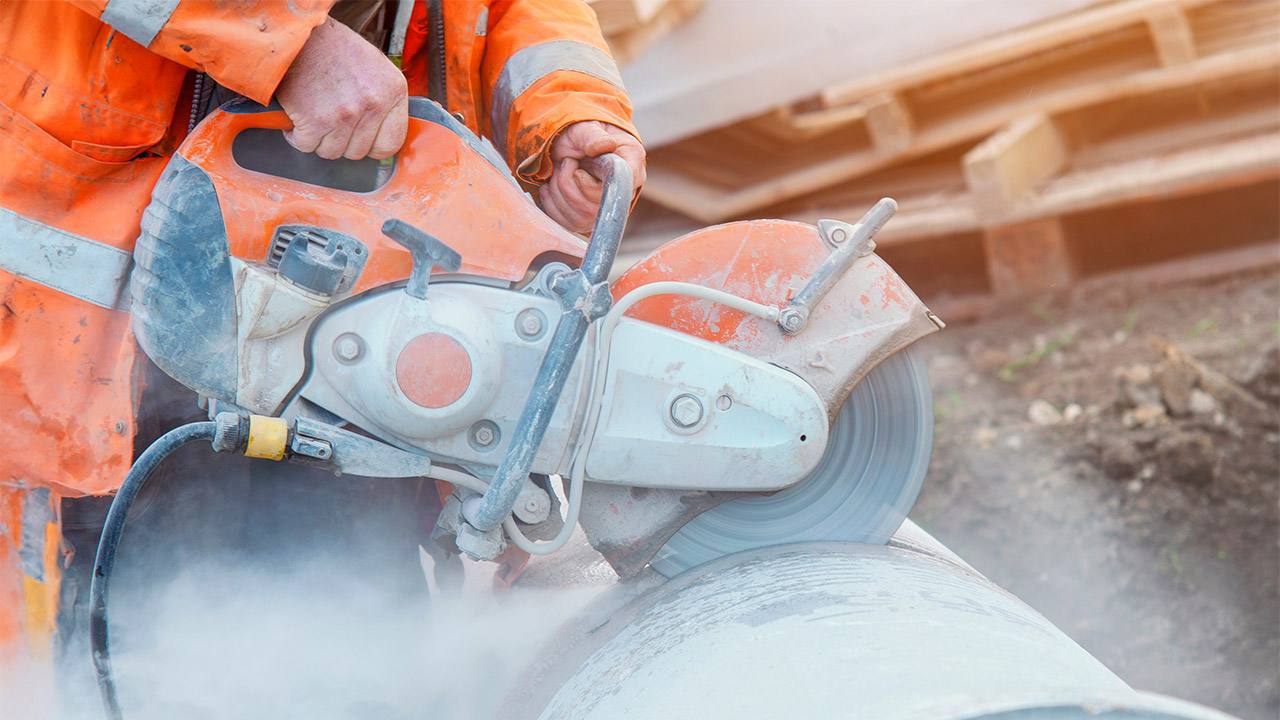 Person using a handheld saw cutting into stone creating dust