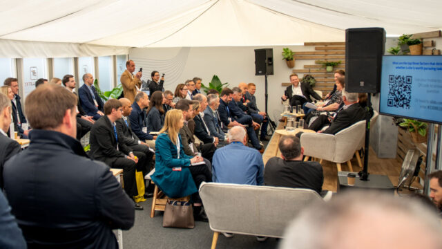 Audience of business people listening to a panel discussion in an exhibition marquee