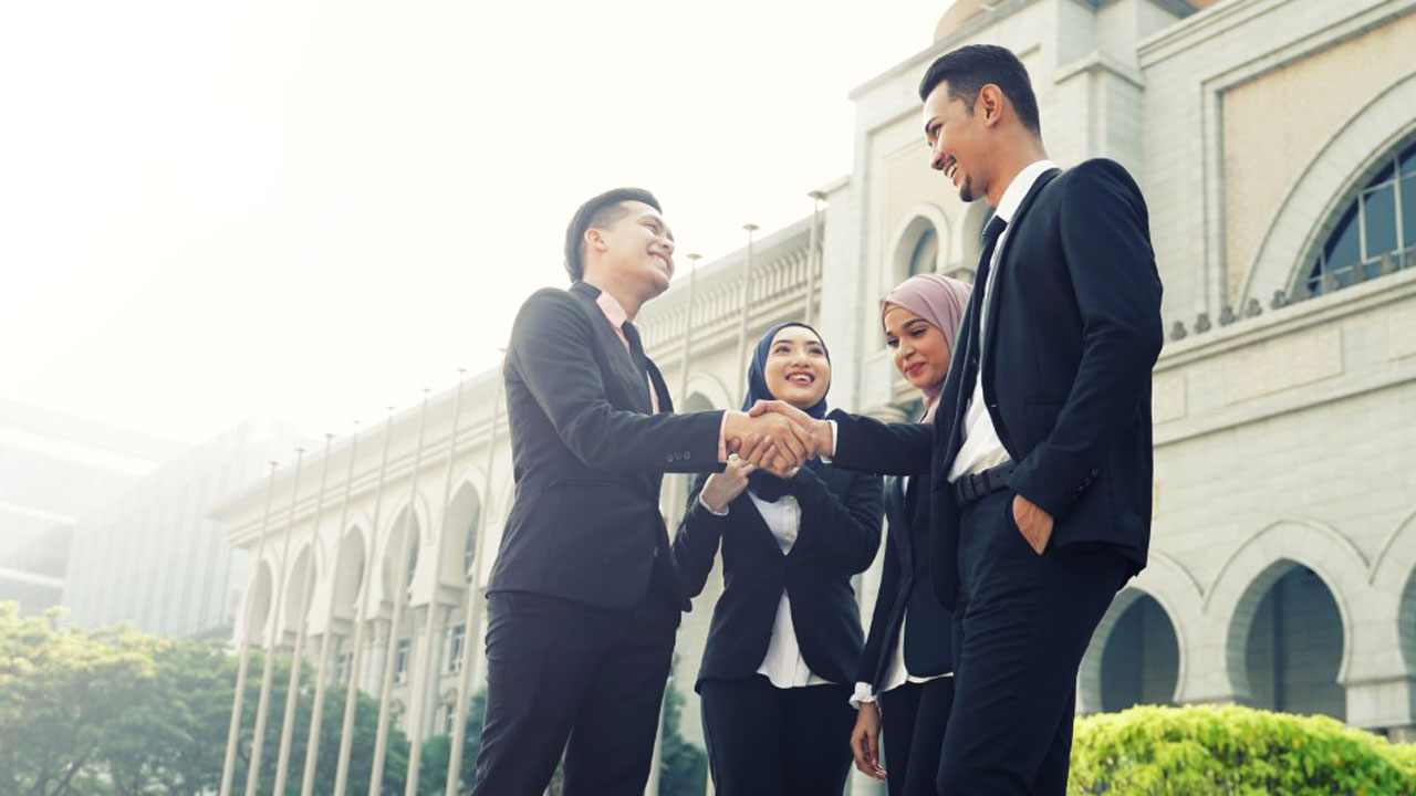 Group of people in suits shaking hands and smiling outside a building