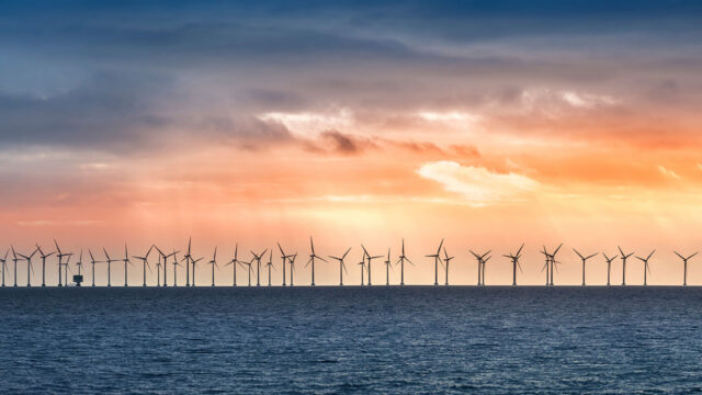 A line of offshore wind turbines with the sun setting behind