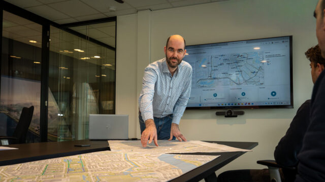 Julian Hartman looks at the camera while he points to maps on a conference table