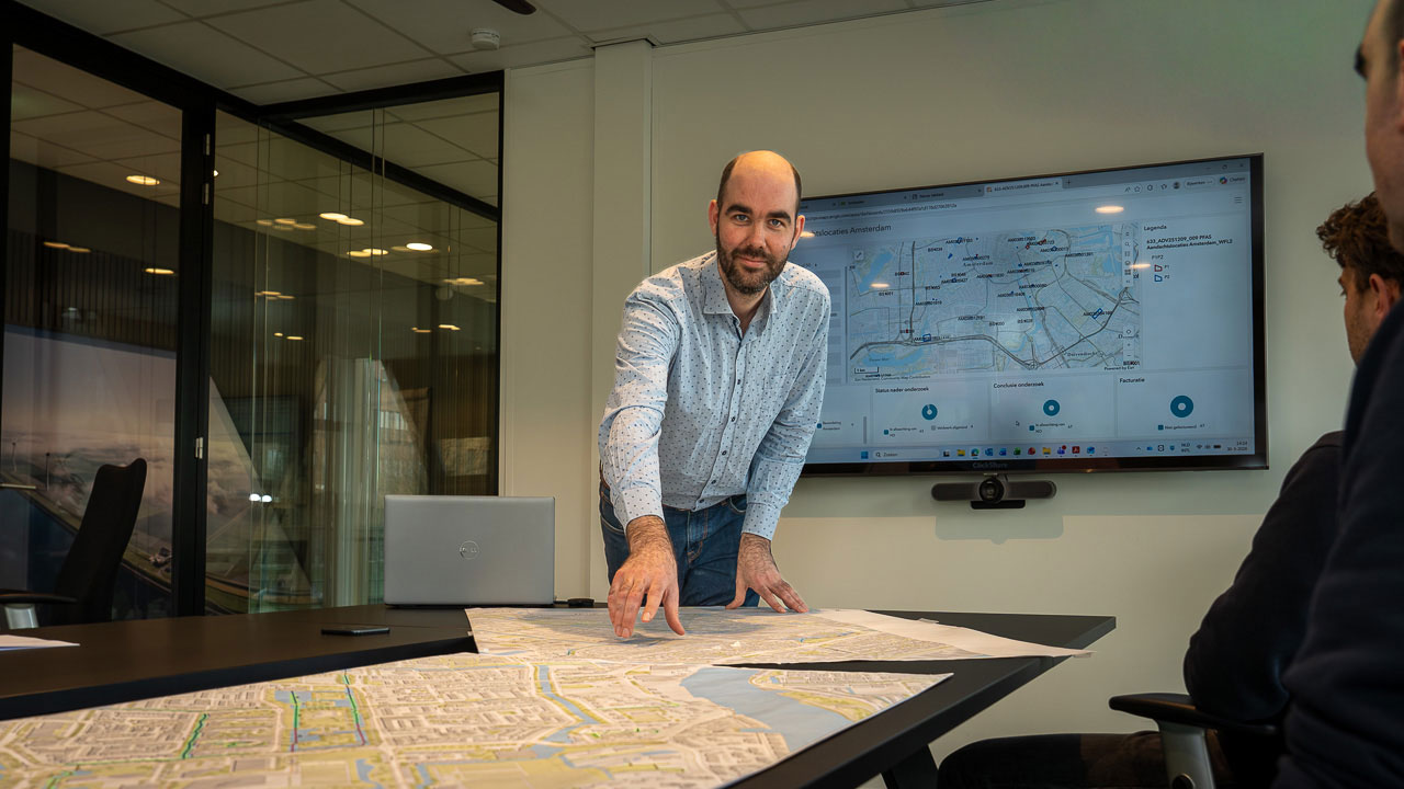 Julian Hartman looks at the camera while he points to maps on a conference table