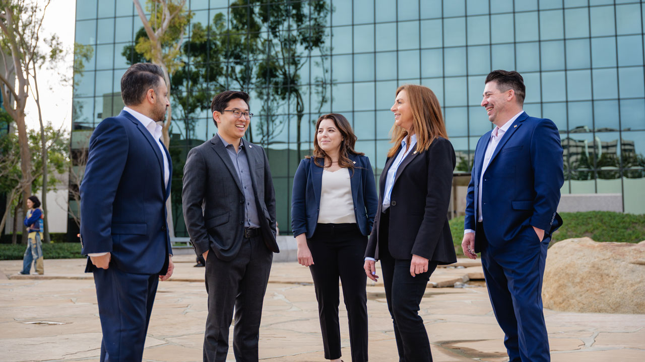 Five business professionals stand and chat outside a modern glass office building