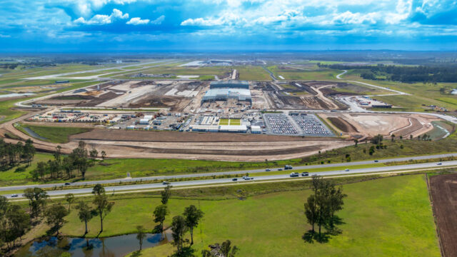 Aerial view of an airport beside a highway under a bright blue sky