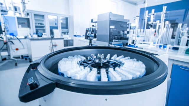 A laboratory centrifuge spins white sample tubes in a bright lab