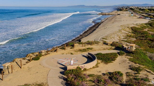 A sunny coastal beach with waves, sand, and a scenic overlook