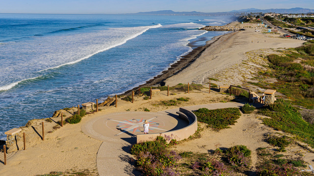 A sunny coastal beach with waves, sand, and a scenic overlook